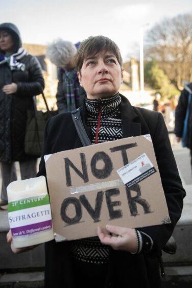 woman holding a cardboard placard which reads 'Not over'.