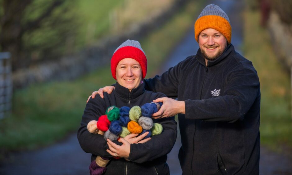 A woman holding colourful yarn and a man holding a skein of yarn wearing knitted hats