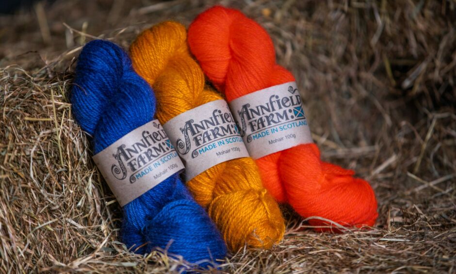 A blue, gold and orange skein of yarn resting on a haybale 