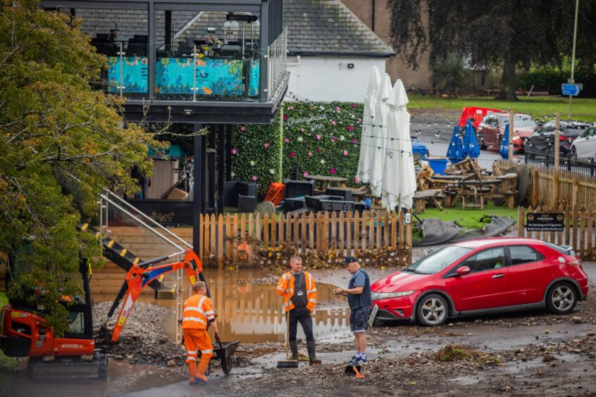 Workers clearing up dirt and mud in submerged car park next to Cherrybank Inn in Perth