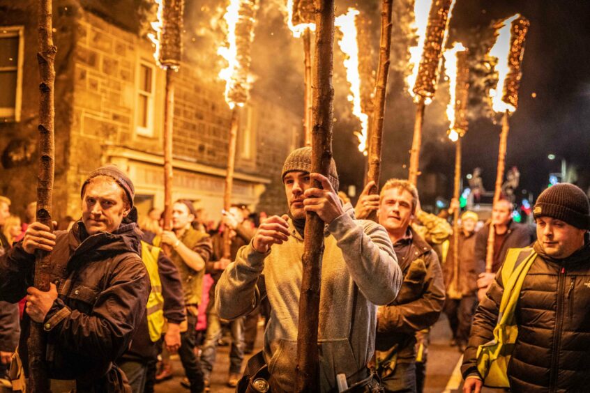 men carry burning torches through the streets of Comrie.