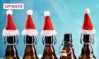 Photo shows five beer bottles, four wearing little Santa hats and one without.