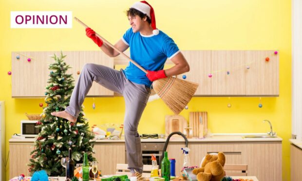 man in a Santa hat with a broom dancing on a messy Christmas dinner table.