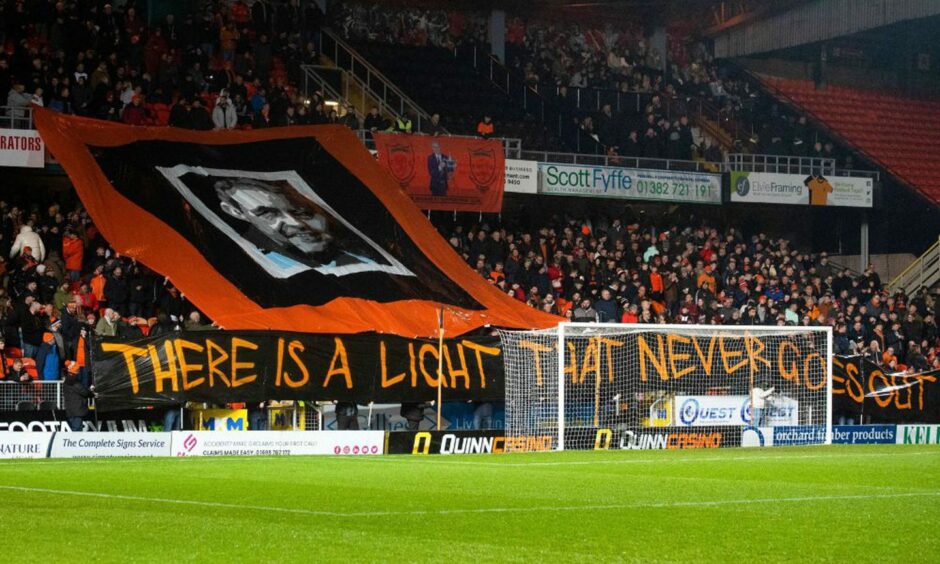 Giant banner in a football stadium showing the face of Jim McLean and the word 'There is a light that never goes out'.
