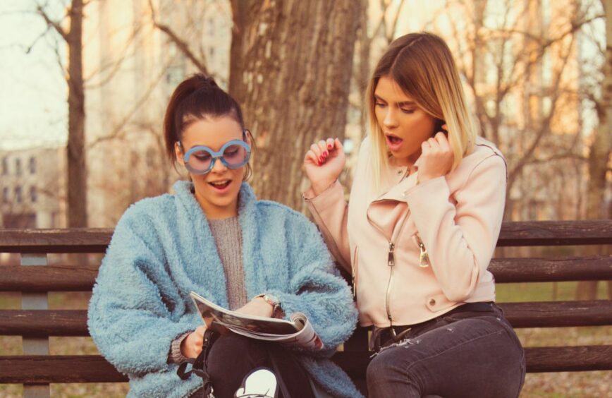 Two young women acting surprised as they read something in a magazine.