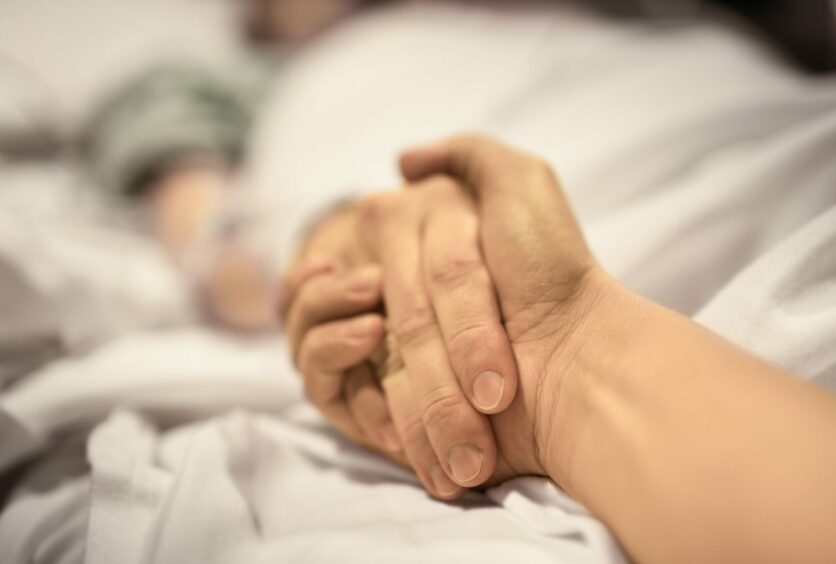 holding the hand of someone in a hospital bed.