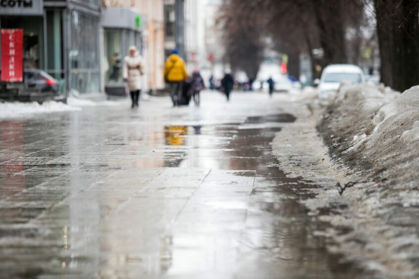 pedestrians walking on pavements with ice piled up by the edge.