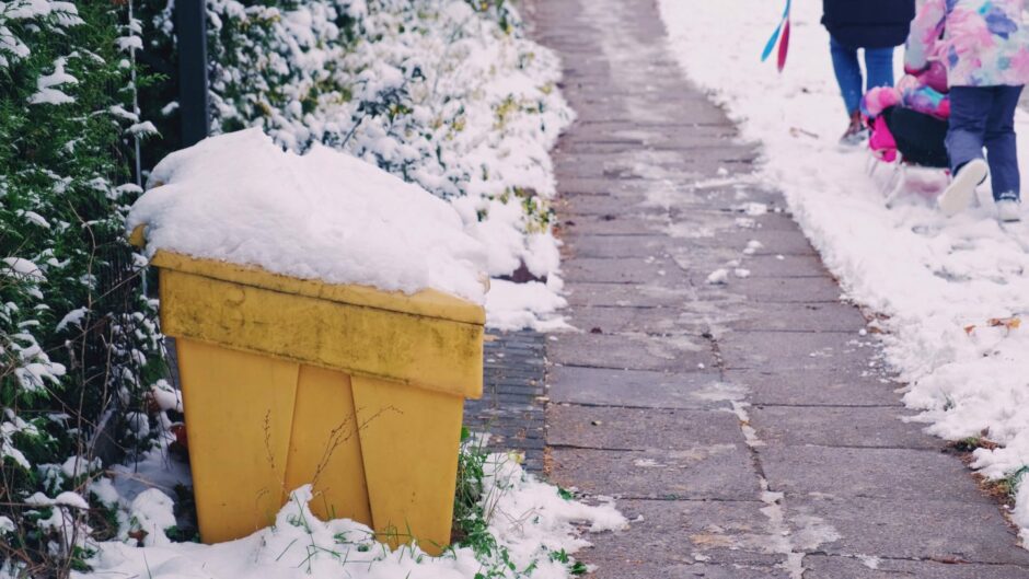 woman and child walking past a grit bin covered in snow.