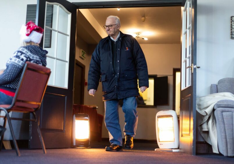elderly man walking into a public building past two electric heaters.