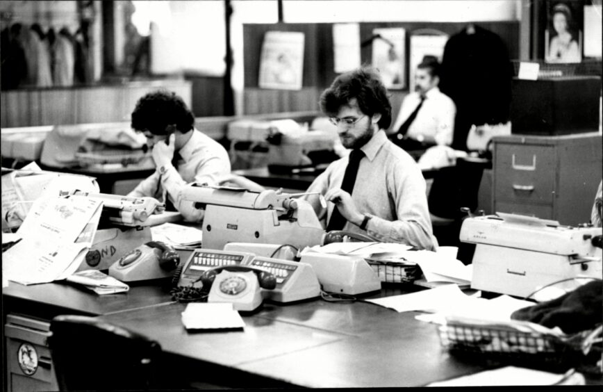 reporters at typewriters in an old-fashioned newsroom.