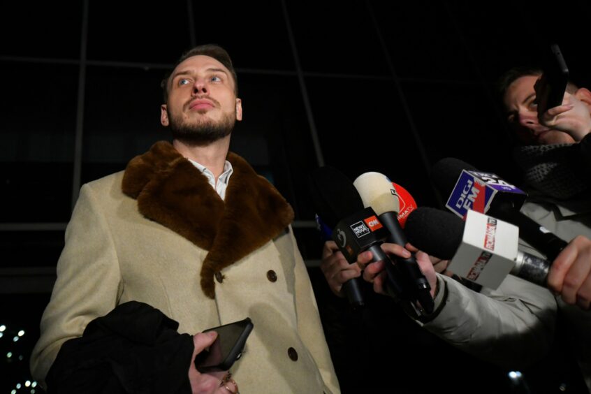 Andrew Tate's lawyer Eugen Vidineac speaks to a crowds of reporters holding microphones.