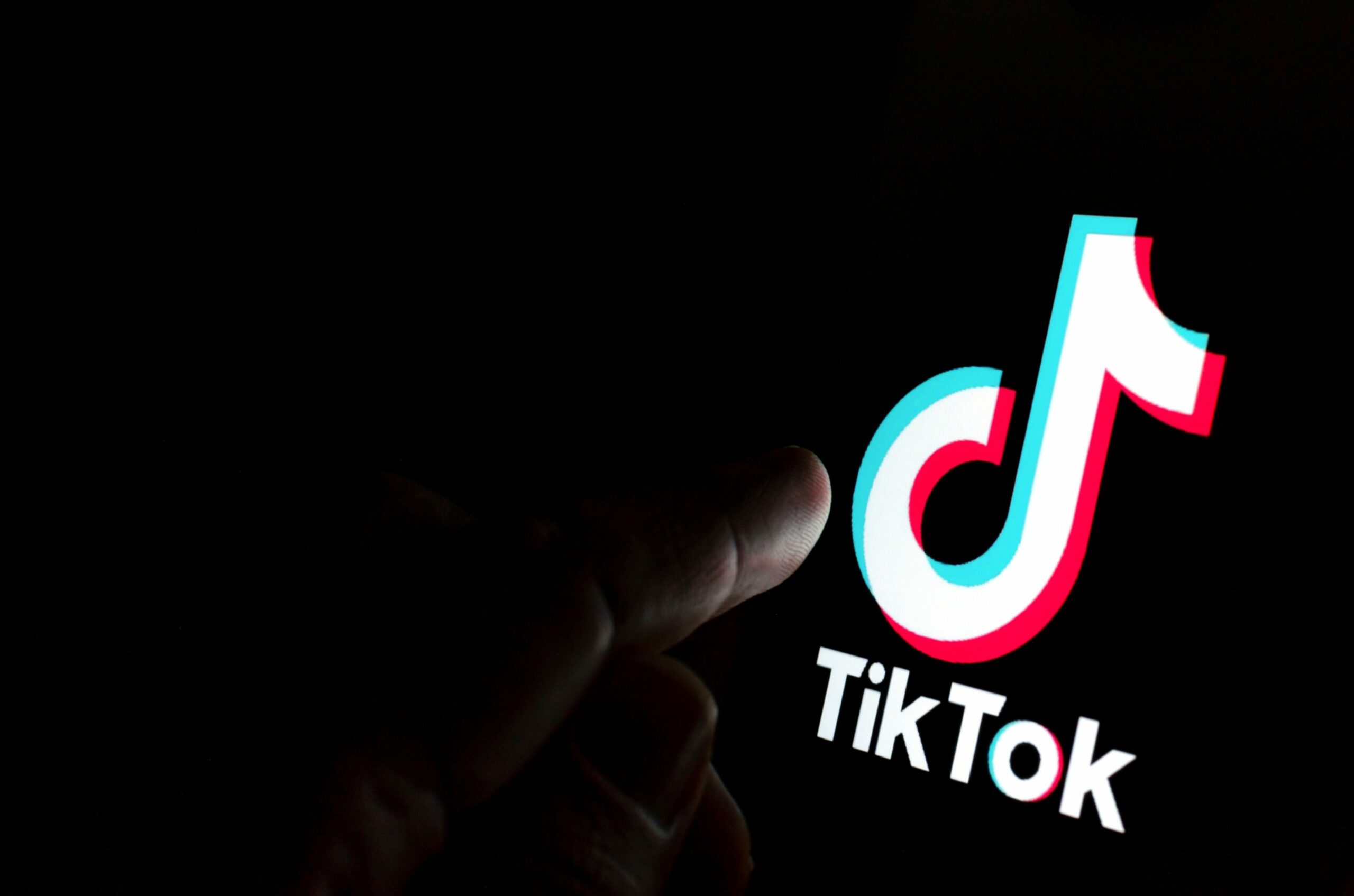 TikTok app logo on screen and a finger pointing at it. 