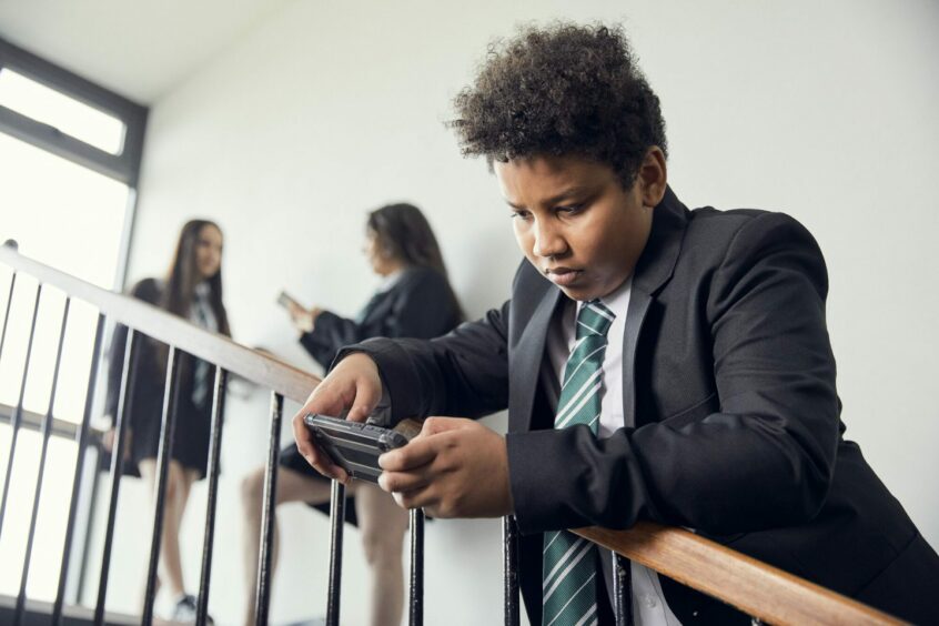 schoolboy looking at mobile phone, with two girls in background