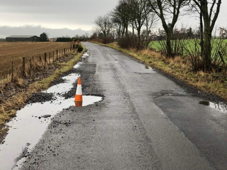 A rural road in Angus with a cone sitting inside a big, water-filled pothole