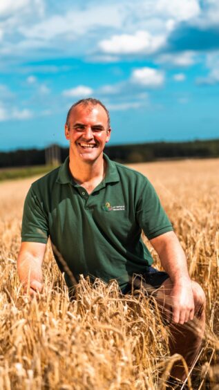 Scottish farmer David Bell in his field, wearing a green polo, with a blue sky overhead.