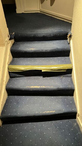 A flight of hotel stairs with tape covering a damaged area.