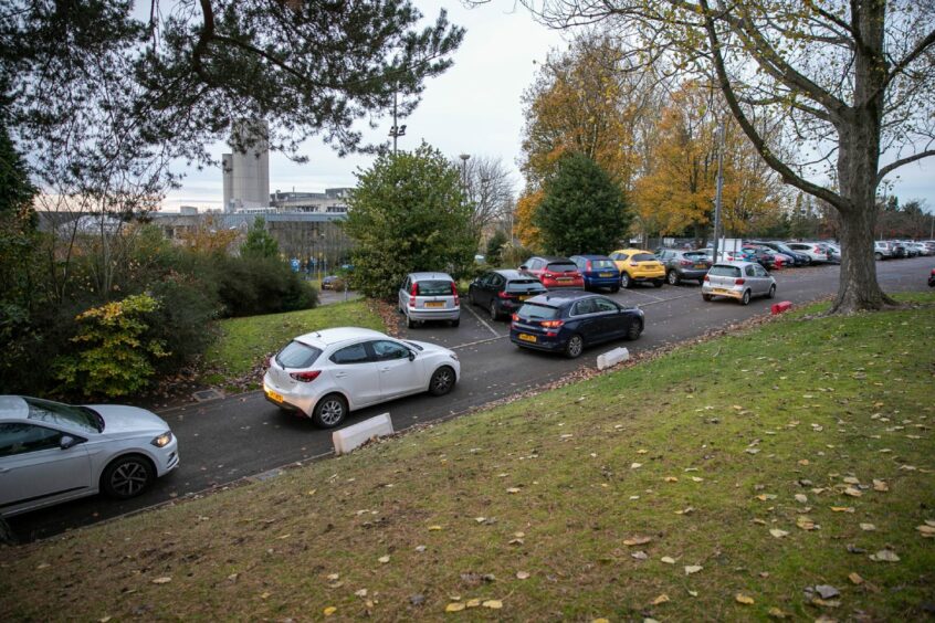 a line of cars driving past full parking spaces at Ninewells Hospital.