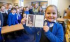 The P4/5 class at Lumphinnans Primary School recently received a message from King Charles. Pictured is: Emily Paterson (8) proudly showing off the royal message as the rest of the class and class teacher Mrs Laurie Main look on. Image: Kenny Smith/DC Thomson