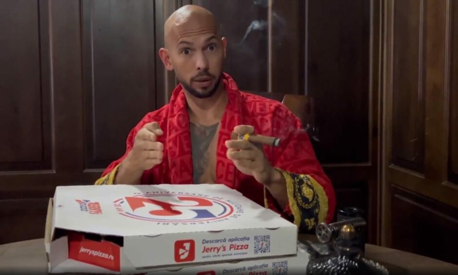 Andrew Tate holding a cigar next to two pizza boxes.