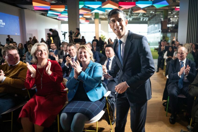 Smiling Rishi Sunak walking through an audience of people applauding.