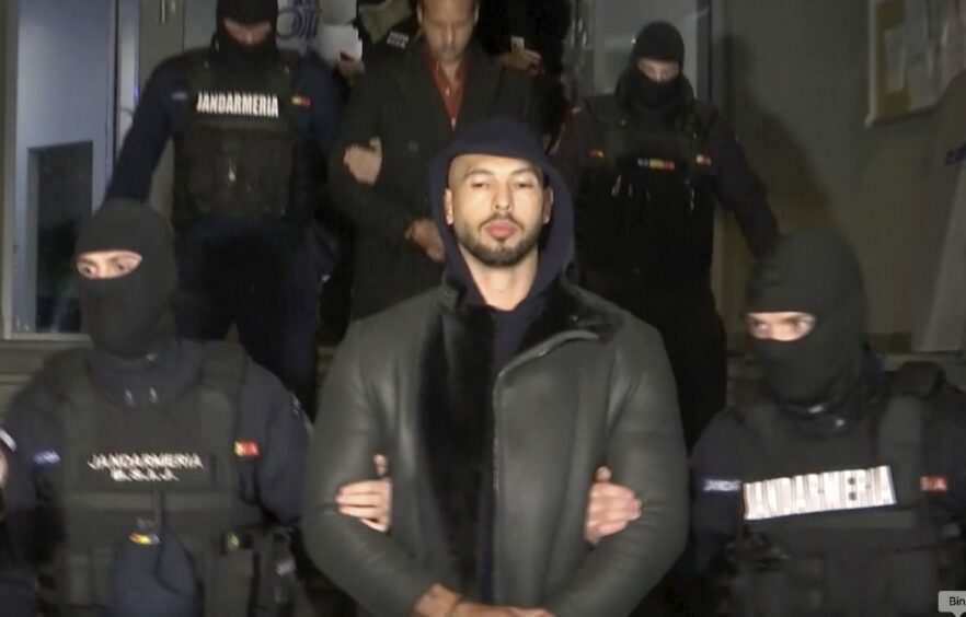 Andrew Tate is led away by masked Romanian police officers.