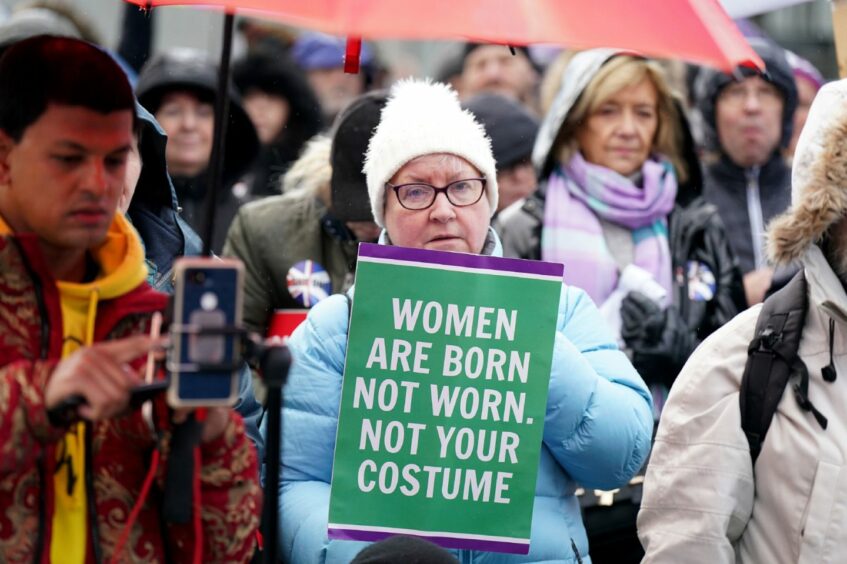 woman holding a sign which reads 'Women are born, not worn. Not your costume'.