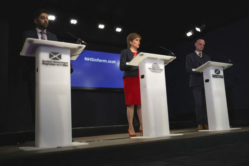 Health Secretary Humza Yousaf, First Minister Nicola Sturgeon and deputy Chief Medical Officer Gregor Smith behind podiums at a press conference.