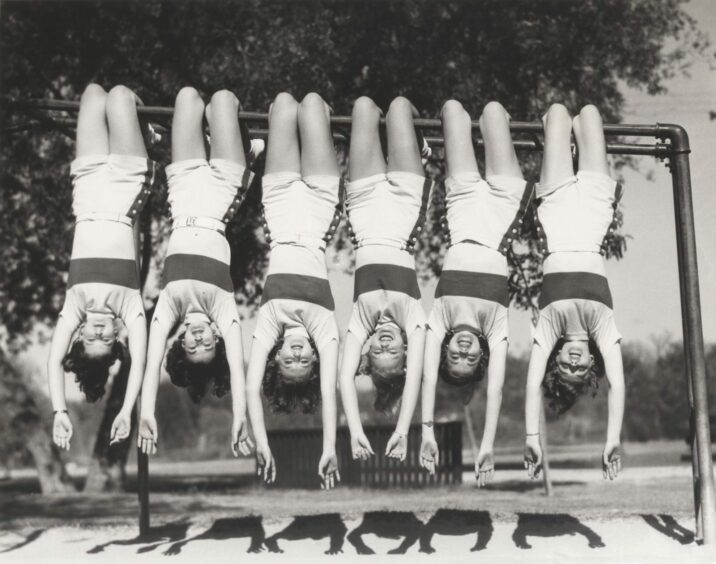 vintage photo of young women hanging from monkey bars.