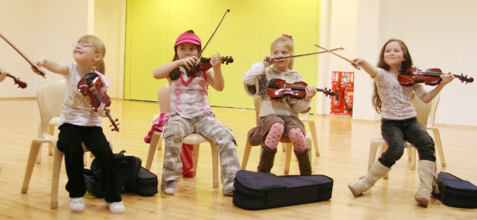 four little girls playing violins in rehearsal