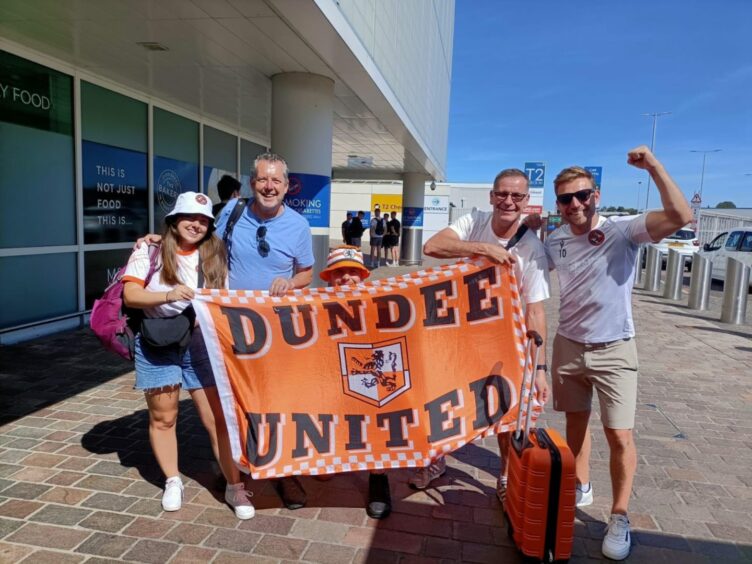 Alistair Heather and friends at an airport holding a Dundee United banner.