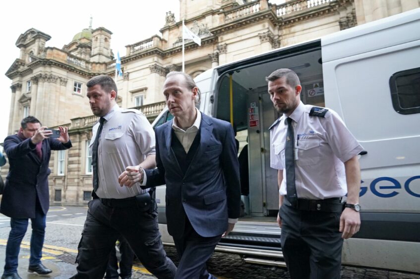 Andrew Innes leaving a van, handcuffed to a security officer.