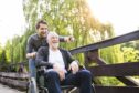a young man enjoys the outdoors with an older man in a wheelchair