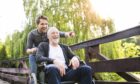 a young man enjoys the outdoors with an older man in a wheelchair