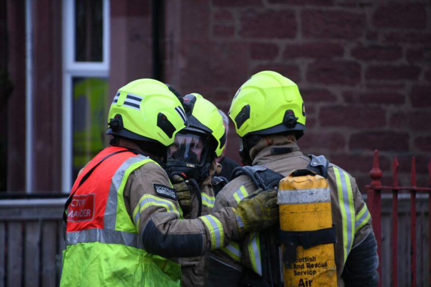 Three firefighters in masks with oxygen cylinders huddled together talking outside a property 