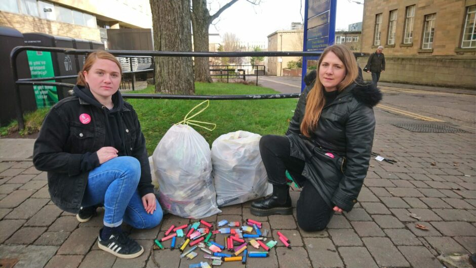 Dundee campaigner Laura Young with North East MSP Mercedes Villalba, kneeling next to a pile of disposable vapes.