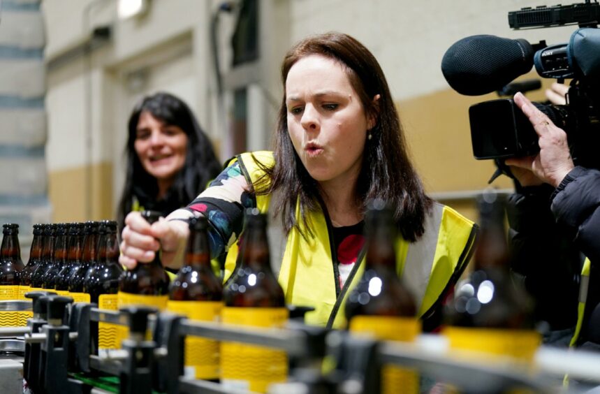 Kate Forbes pulling a face next to a production line of beer bottles on a brewery visit.