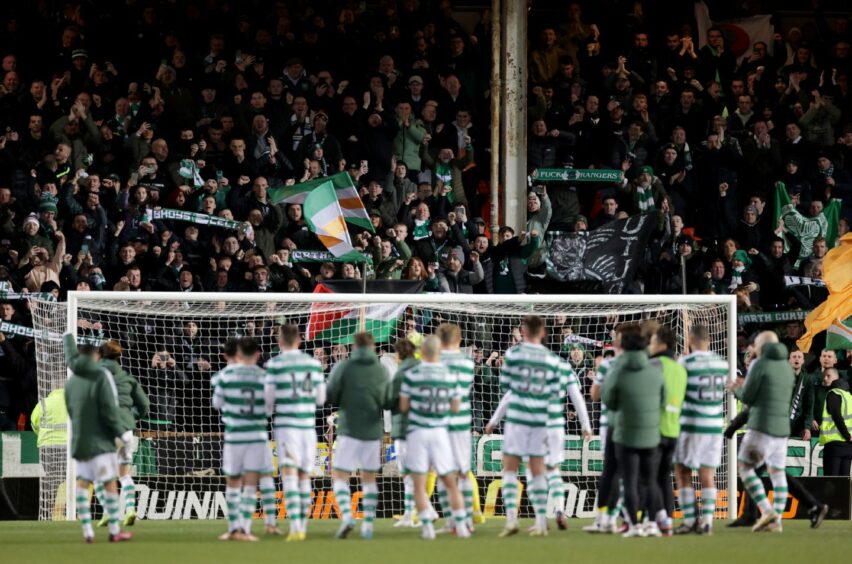 Celtic players on the pitch at Tannadice with a stand full of fans behind them.