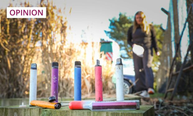 a row of disosable vapes on the pavement with a woman walking past them.