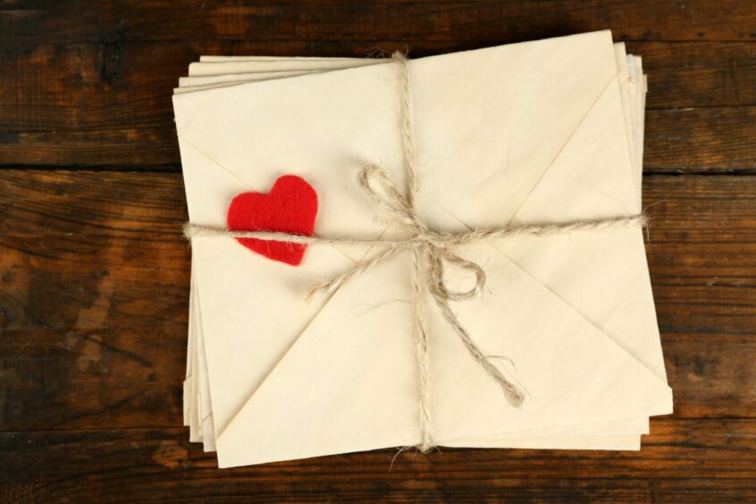 A pile of envelopes, tied with string and a red heart on top.