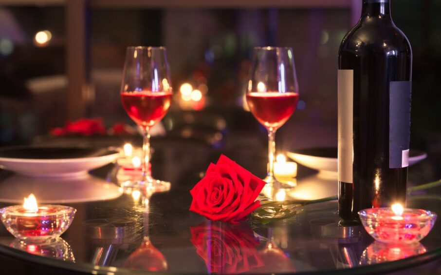 Restaurant table set for two, with red roses and flickering candles.