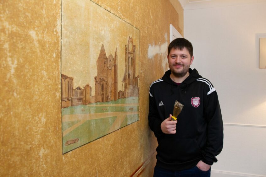 Couple uncover Arbroath Abbey mural on living room wall. 