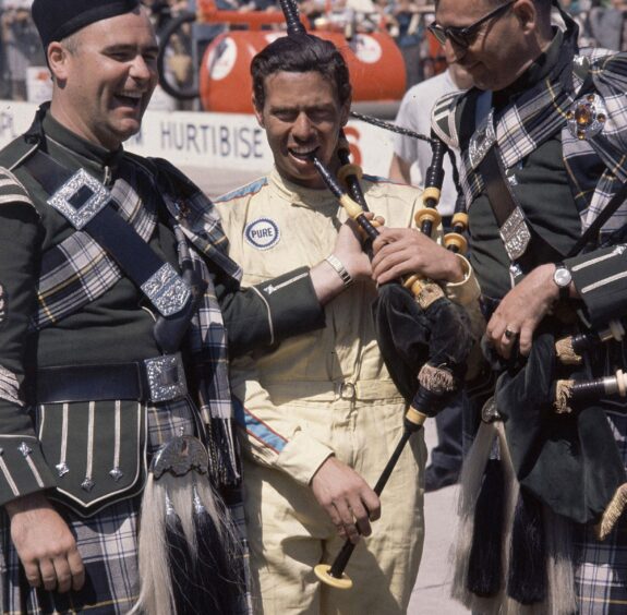 Jim Clark tries a bag pipe with two of his countrymen in traditional tartan dress at Indianapolis Motor Speedway.