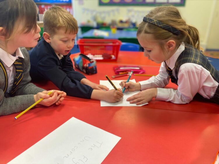 Pupils draw on a piece of paper on a red table as they make P1 transition from nursery