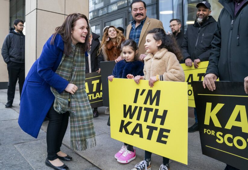 Kate Forbes laughing with little girls holding an 'I'm with Kate' placard.