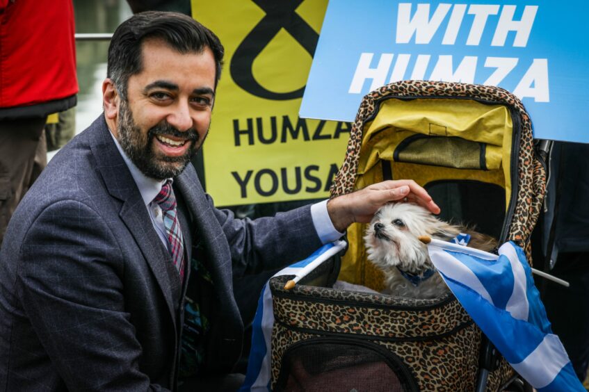 Humza Yousaf petting a small dog in a pram with a Scottish saltire flag poking out of it.