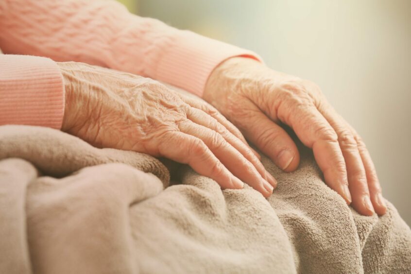 Image showing an older person's hands on their blanketed knees.