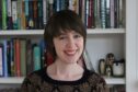 Author JJA Harwood is pictured smiling in a head and shoulders shot. She is in front of a bookcase.