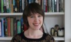 Author JJA Harwood is pictured smiling in a head and shoulders shot. She is in front of a bookcase.