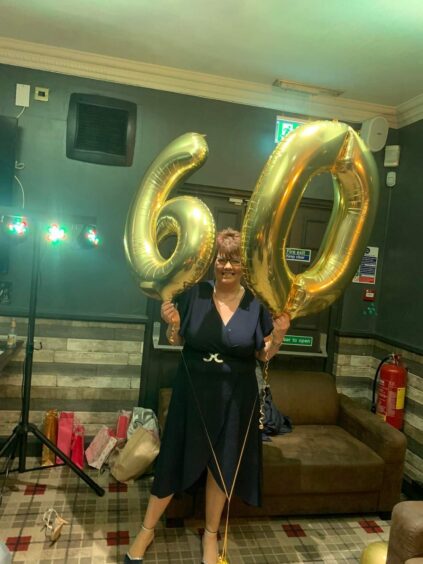 Lorna Mallis holding 60th birthday balloons.