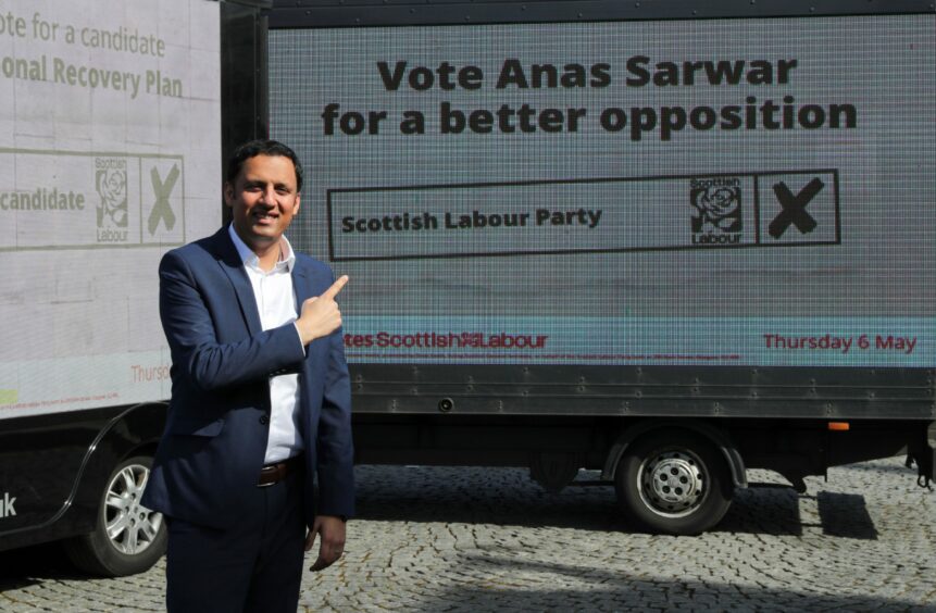 Anas Sarwar next to a billboard which reads 'Vote Anas Sarwar for a better opposition: Scottish Labour Party'.
